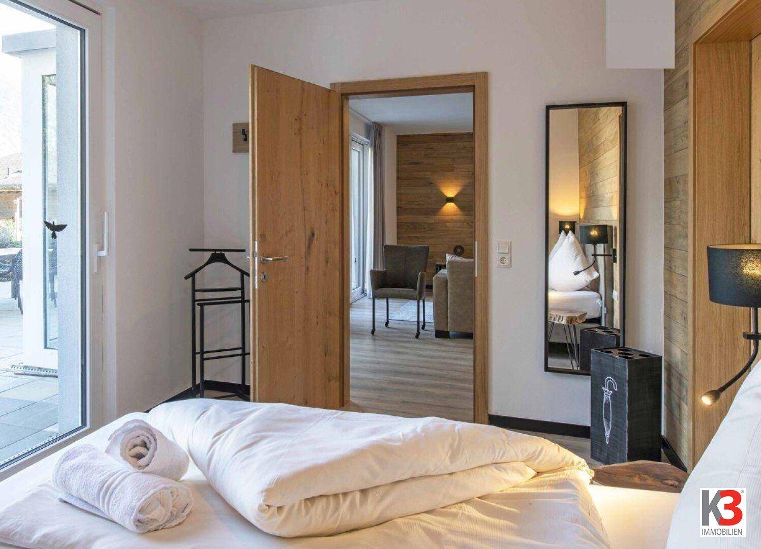 Helles Schlafzimmer mit Zugang zur Terrasse, Holztür und modernem Spiegel.
