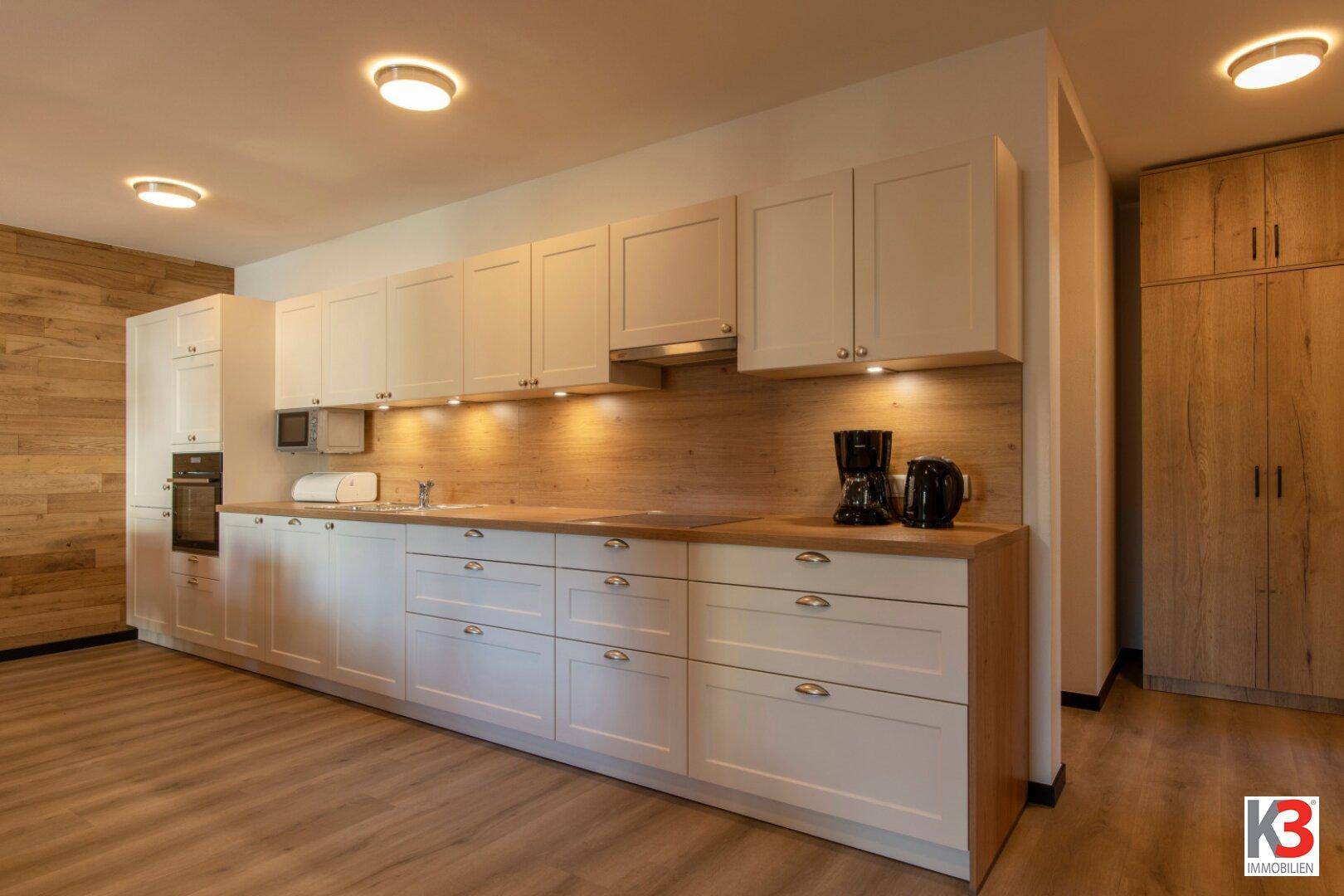 Moderne Einbauküche mit weißen Schränken, Holz-Arbeitsplatte und integrierten Geräten.