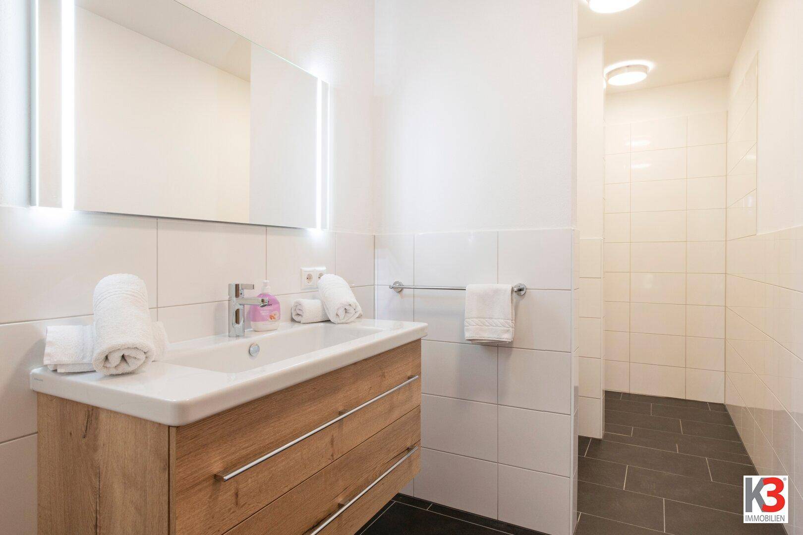 Modernes Badezimmer mit Holzwaschtisch, großem Spiegel und begehbarer Dusche.