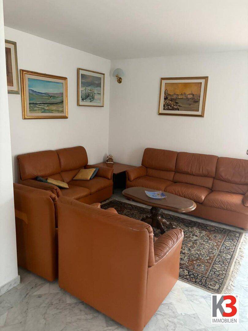 Komfortables Wohnzimmer mit braunen Ledersofas, Marmorboden und Kunstwerken an den hellen Wänden.