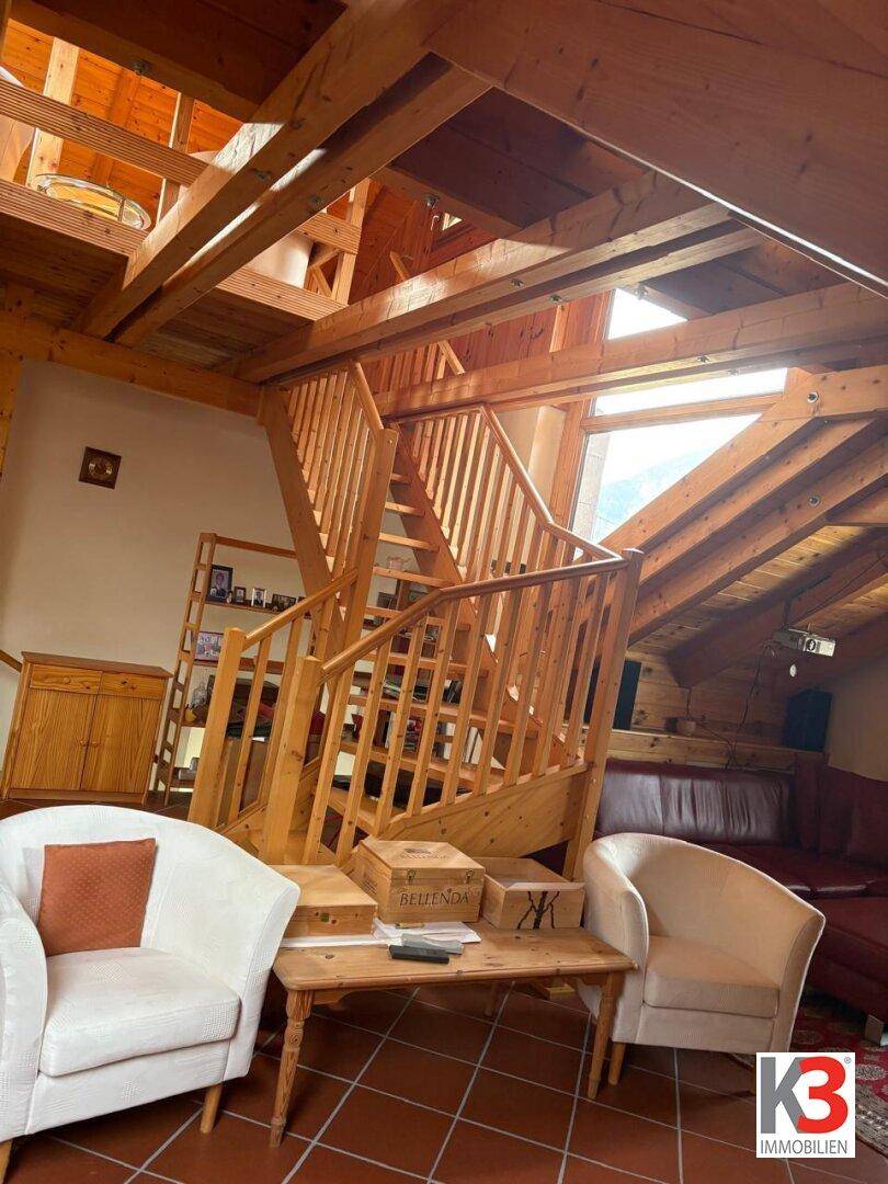 Offener Wohnbereich mit beeindruckender Holztreppe, sichtbaren Dachbalken und hohen Decken.