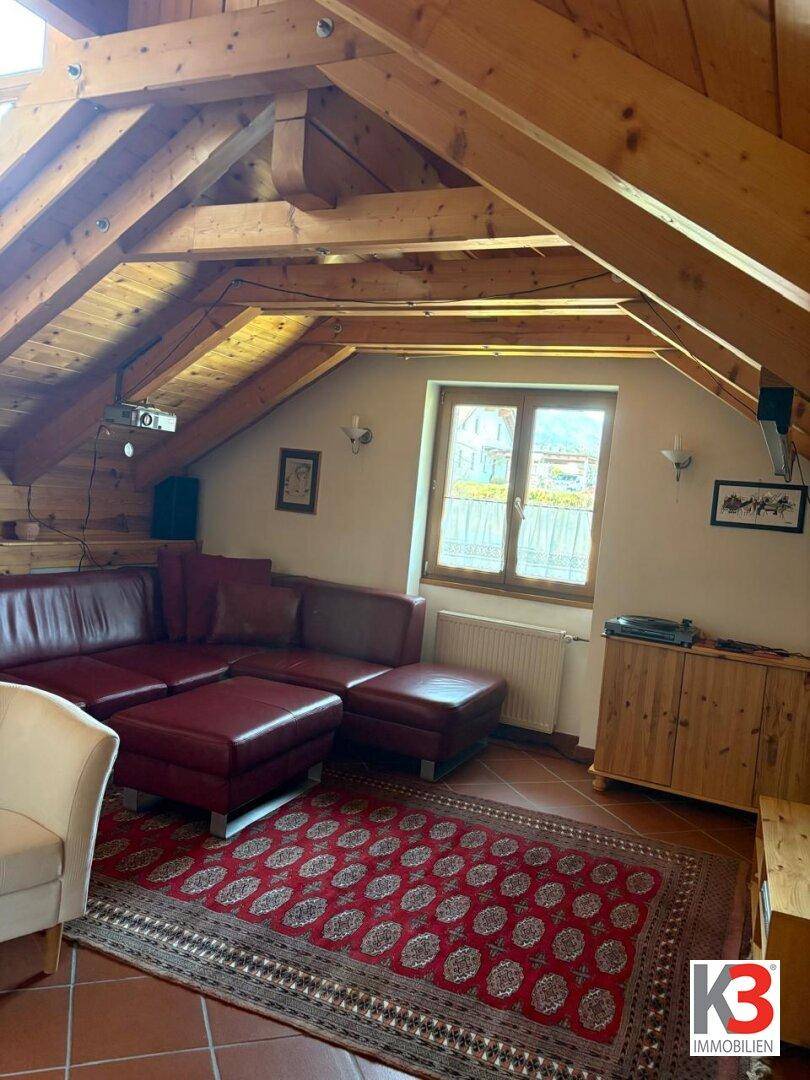 Gemütlicher Wohnbereich im Dachgeschoss mit schrägen Holzdecken, rotem Ledersofa und Fenster.