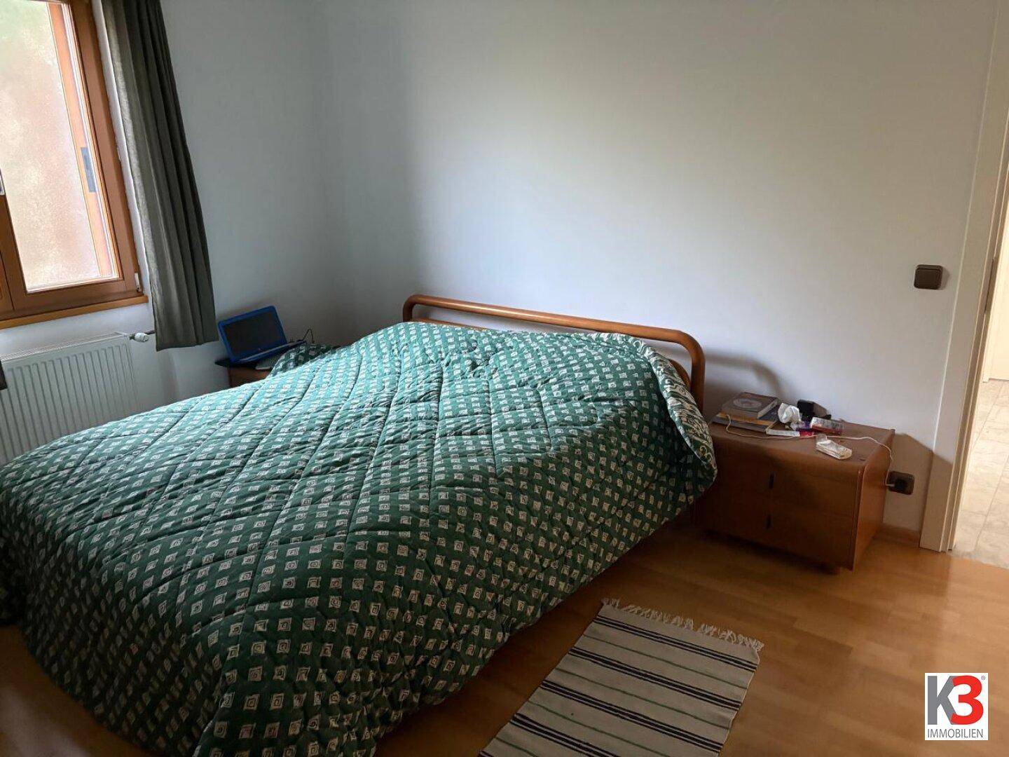 Schlafzimmer mit Holzboden, einem Bett und einem Fenster, das für natürliches Licht sorgt.