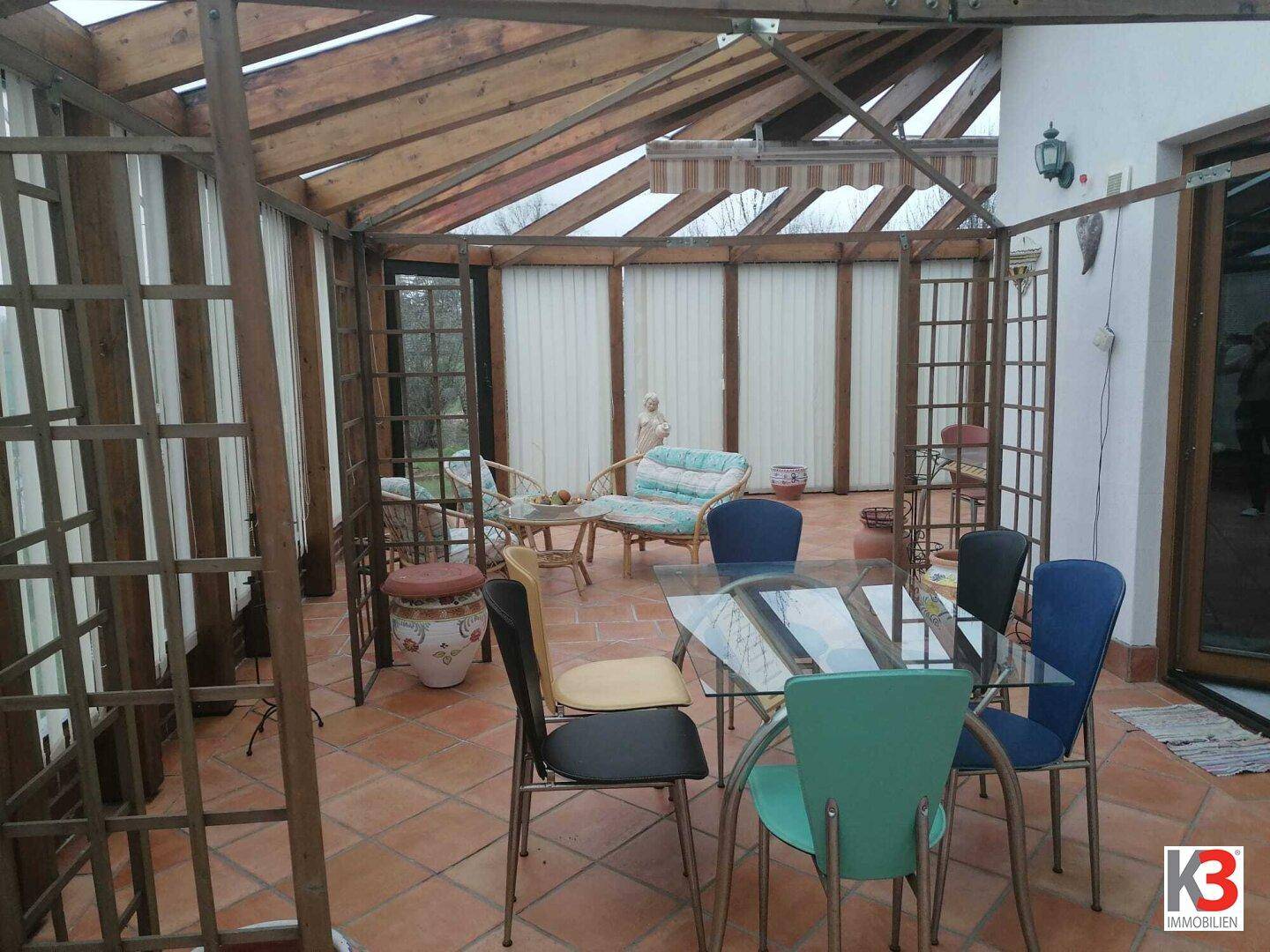 Gemütlicher Wintergarten mit Holzkonstruktion, Terracotta-Boden und Sitzgelegenheiten für entspannte Stunden.
