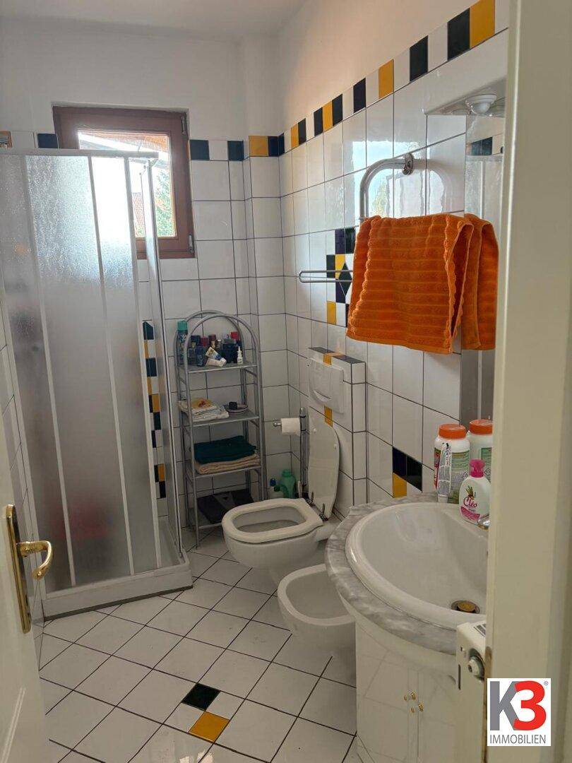 Badezimmer mit farbenfrohen Fliesen in Weiß, Gelb und Schwarz, Dusche, Bidet und Fenster.