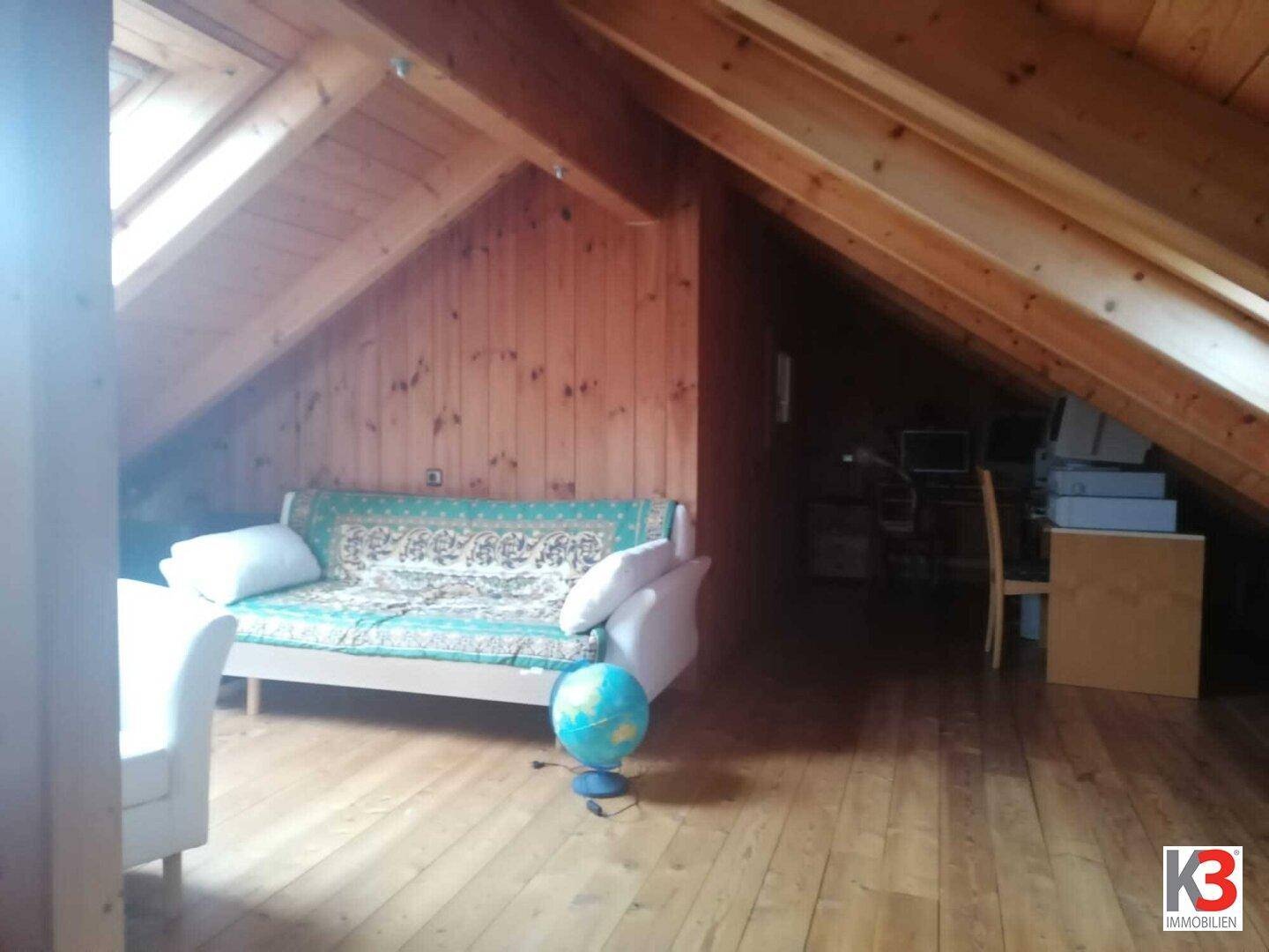 Geräumiger Dachboden mit Holzverkleidung, Holzboden und einem Sofa, ideal als zusätzlicher Wohnraum.