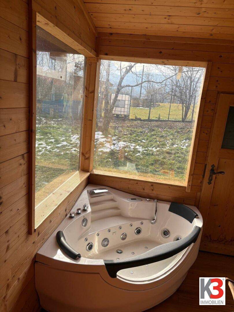 Eck-Whirlpool in einem Holzraum mit großen Fenstern und Blick ins Grüne.