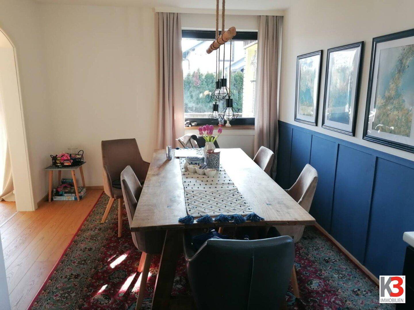 Heller Essbereich mit Holztisch, blauer Wandverkleidung und Blick ins Grüne.