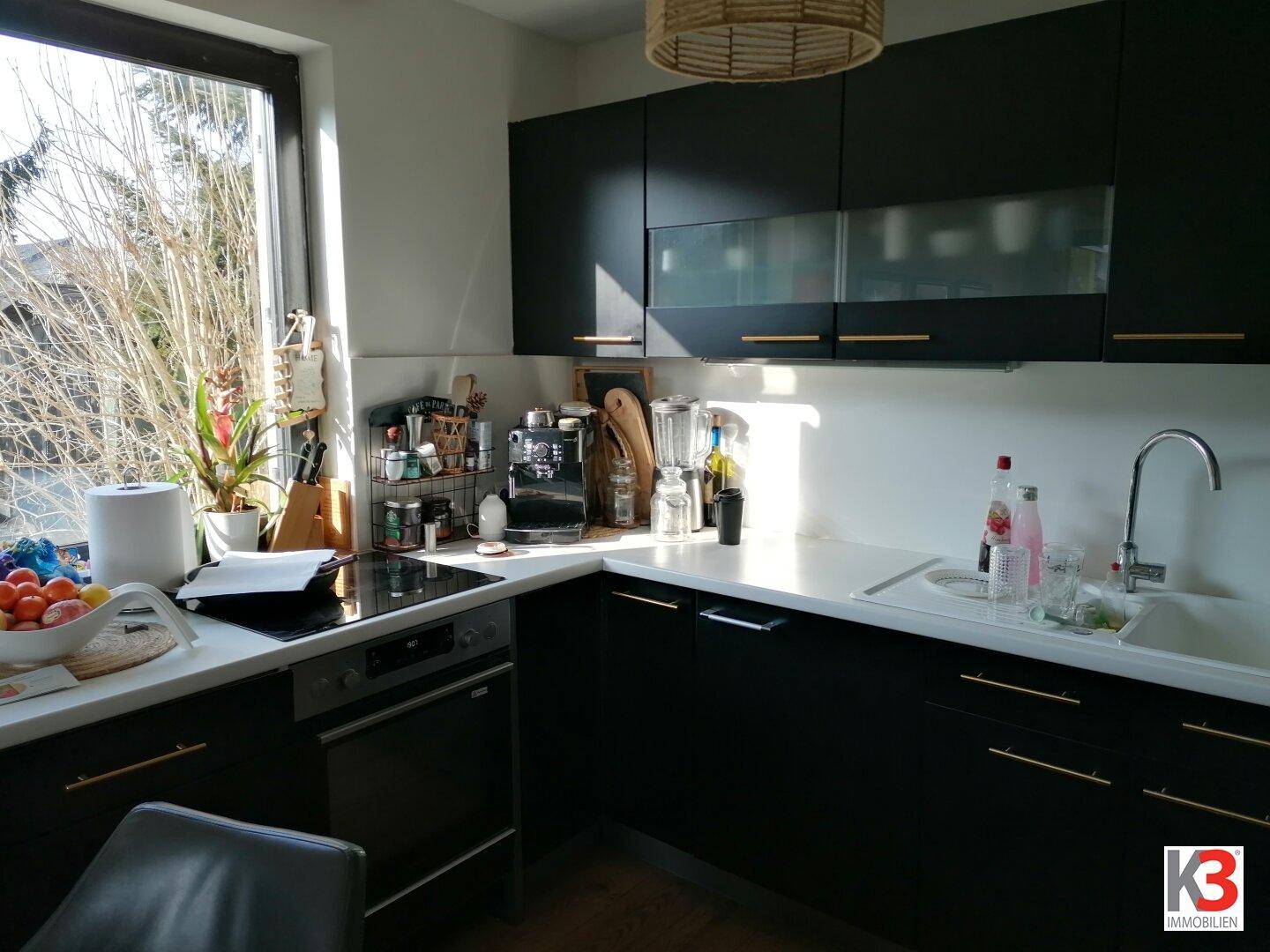 Moderne schwarze Küche mit weißen Arbeitsplatten, integrierten Geräten und großem Fenster.
