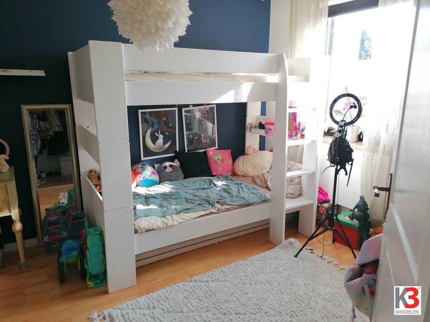 Helles Kinderzimmer mit weißem Etagenbett, blauer Akzentwand und Holzboden.