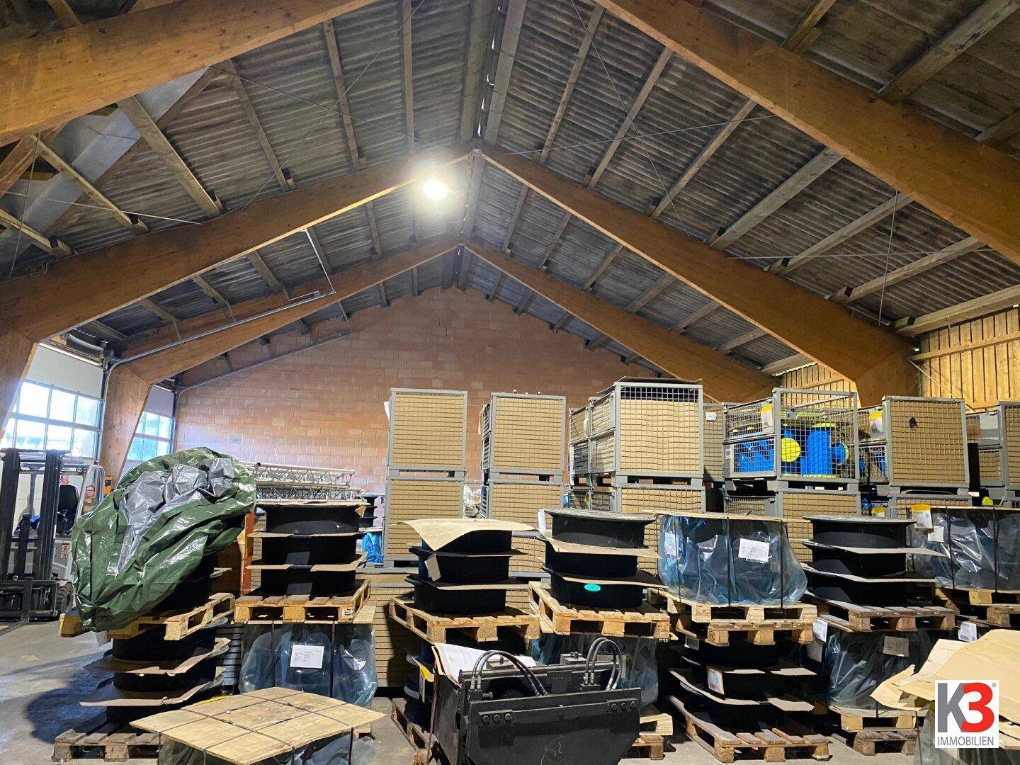 Große Lagerhalle mit hohen Holzdecken, viel Stauraum und natürlichem Lichteinfall durch Fenster, optimal für gewerbliche Nutzung.
