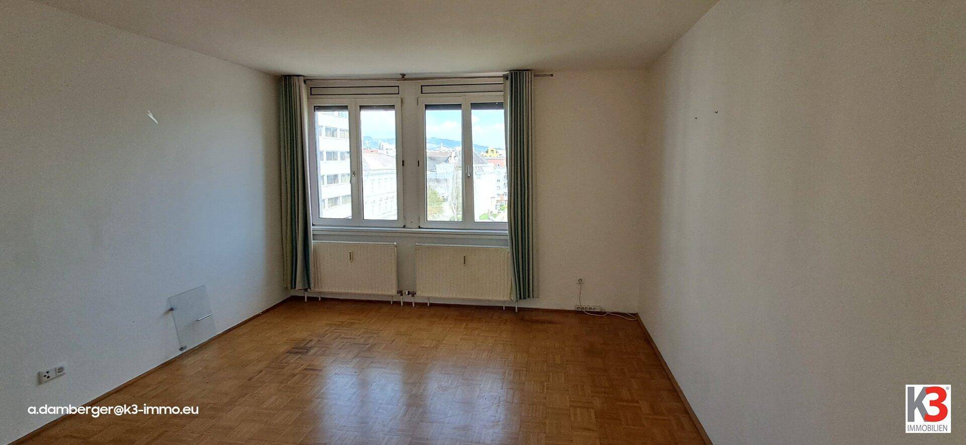 Heller Wohnraum mit Parkettboden und großen Fenstern, der viel Tageslicht hereinlässt.
