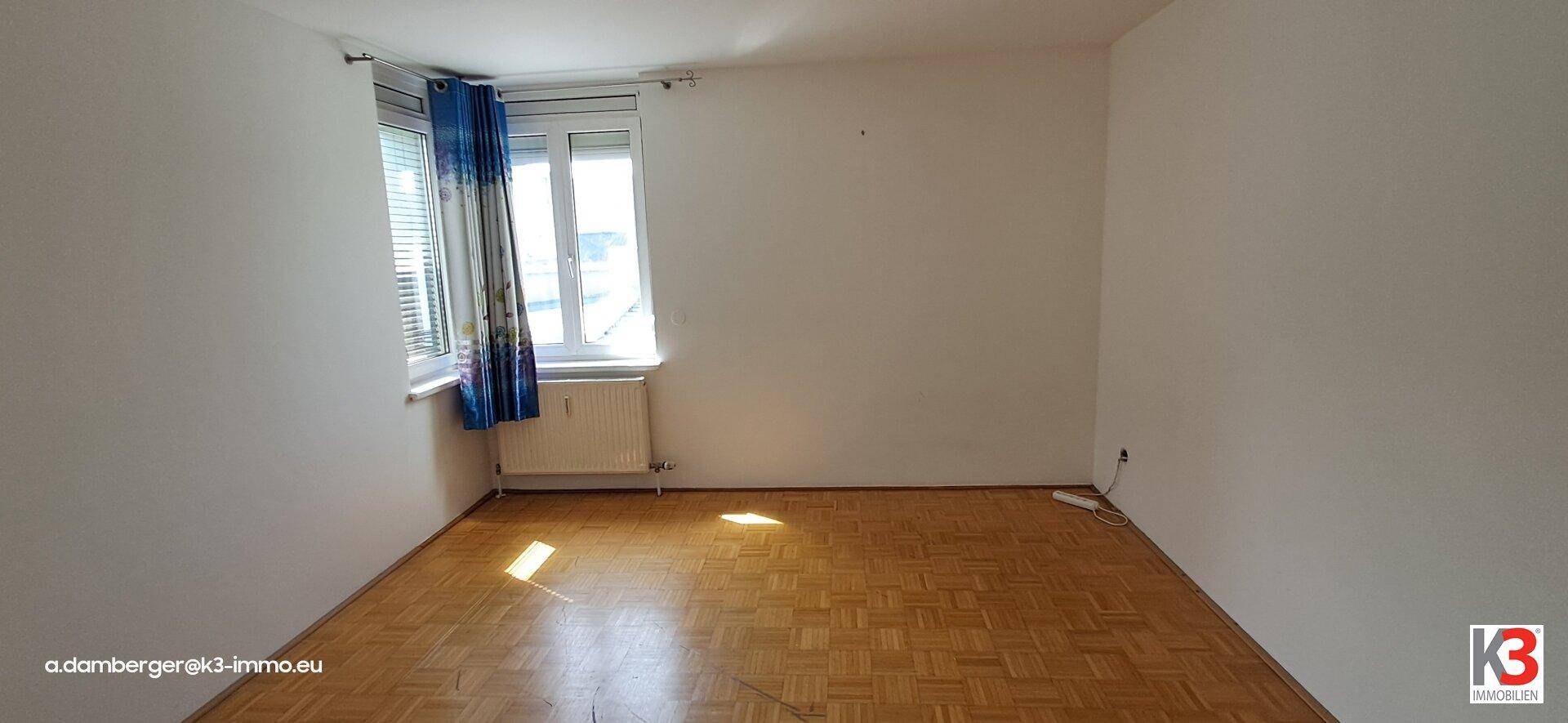 Helles Schlafzimmer mit Parkettboden und Fenster, das viel Tageslicht in den Raum bringt.