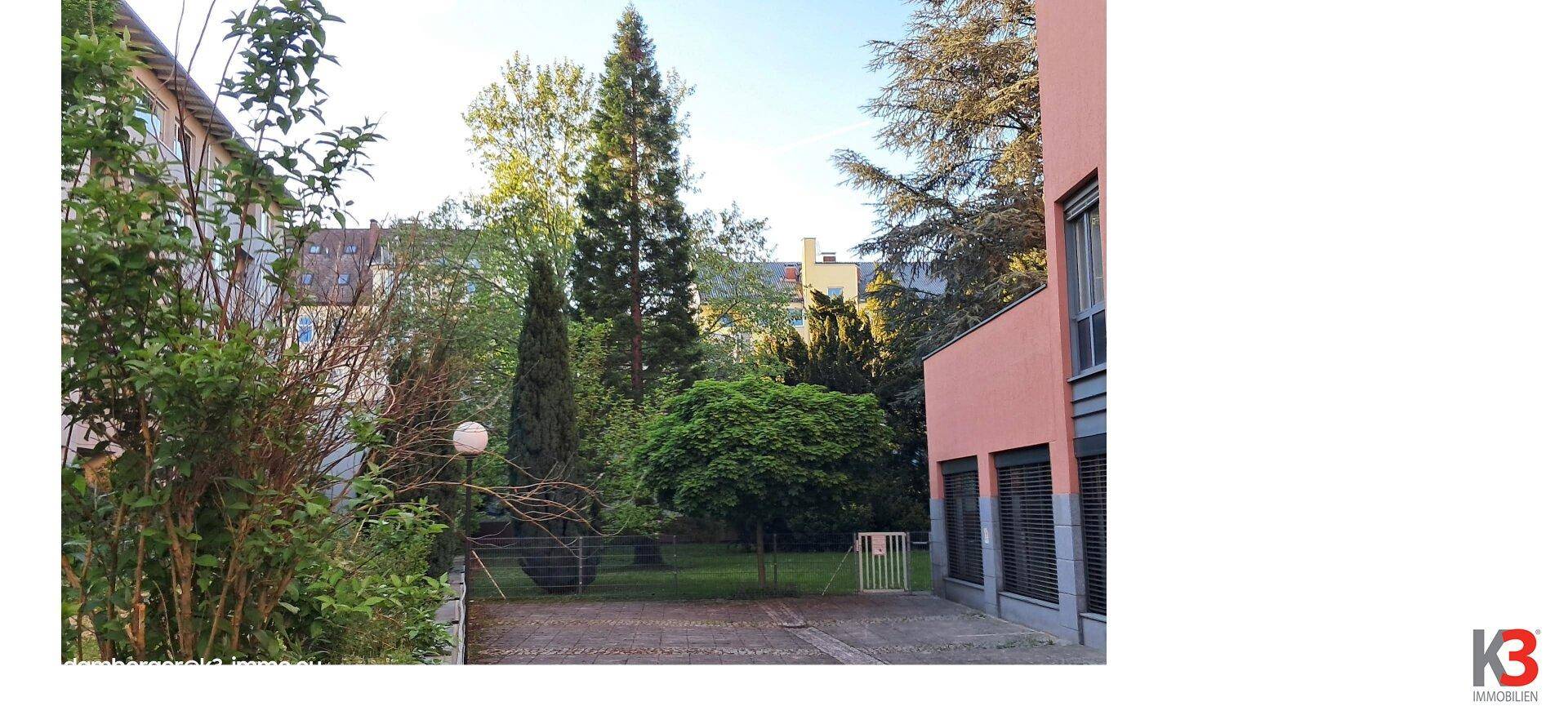 Grüner Gartenbereich mit Bäumen und Sträuchern, umgeben von Wohngebäuden.