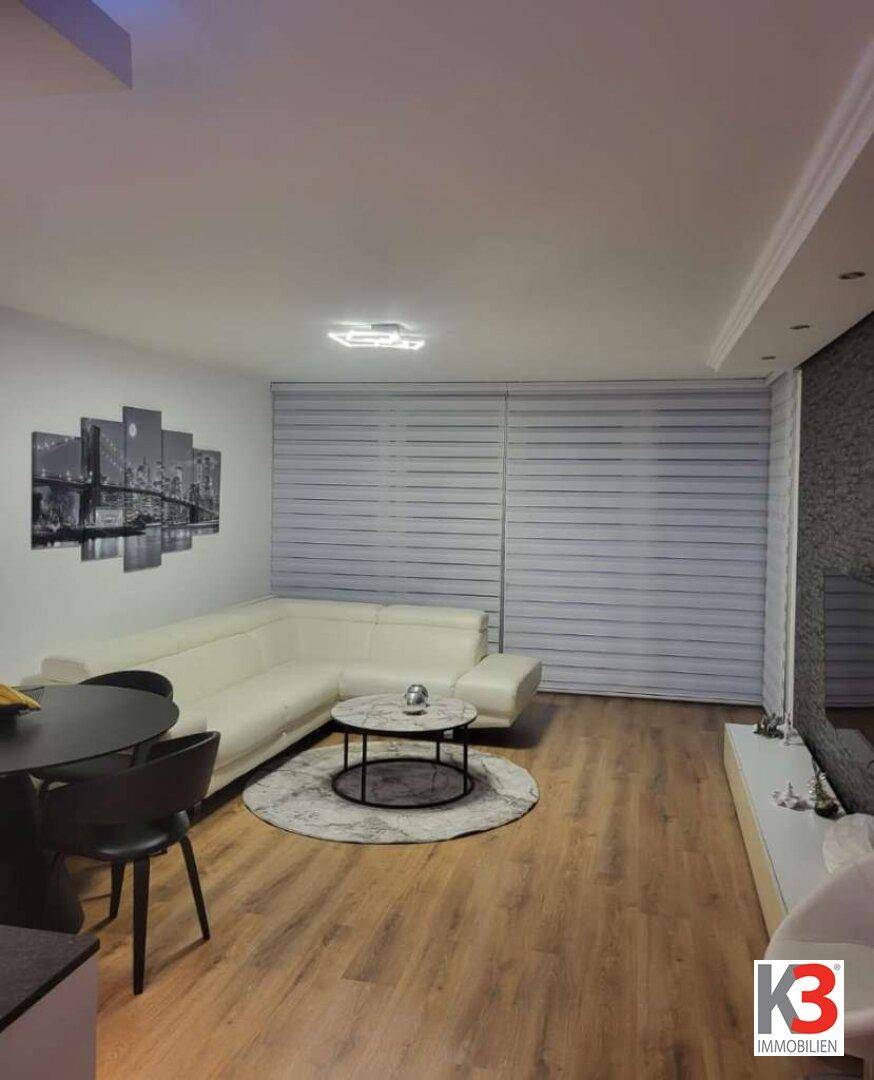 Gemütliches Wohnzimmer mit großem Ecksofa, Holzboden und modernen Fensterjalousien.