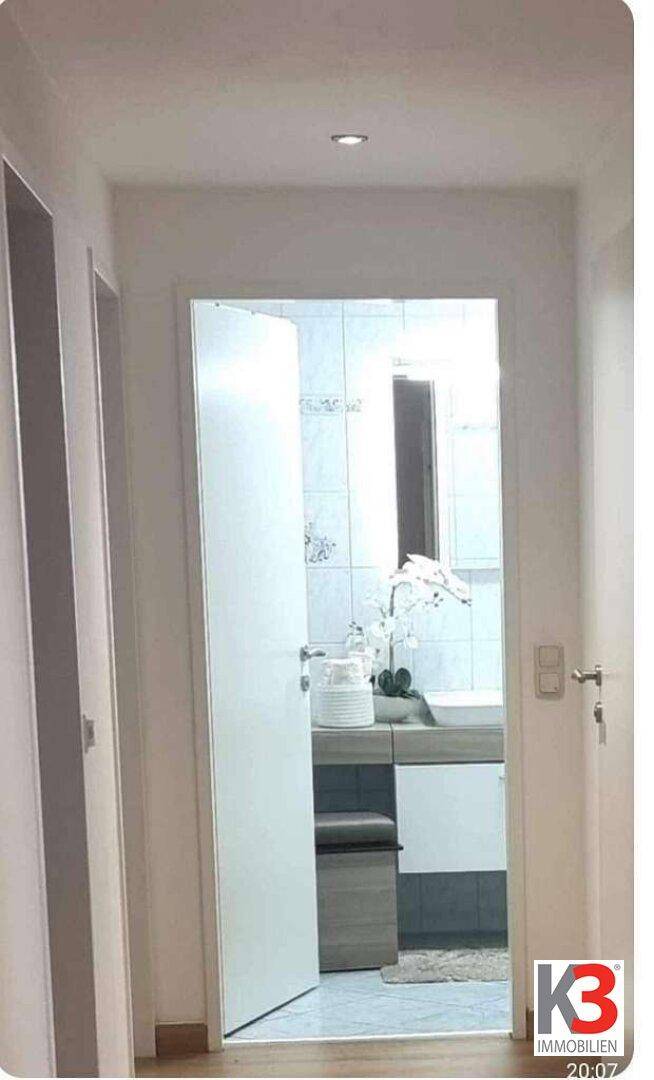 Heller Flur mit Blick in ein Badezimmer, das mit weißen Fliesen und einem modernen Waschtisch ausgestattet ist.