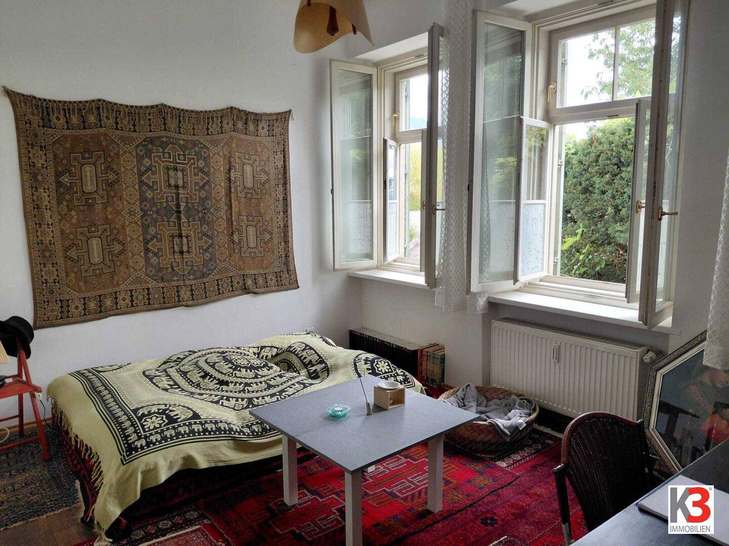 Schlafzimmer mit Einzelbett, Teppichboden und Blick auf den Garten durch die Fenster.