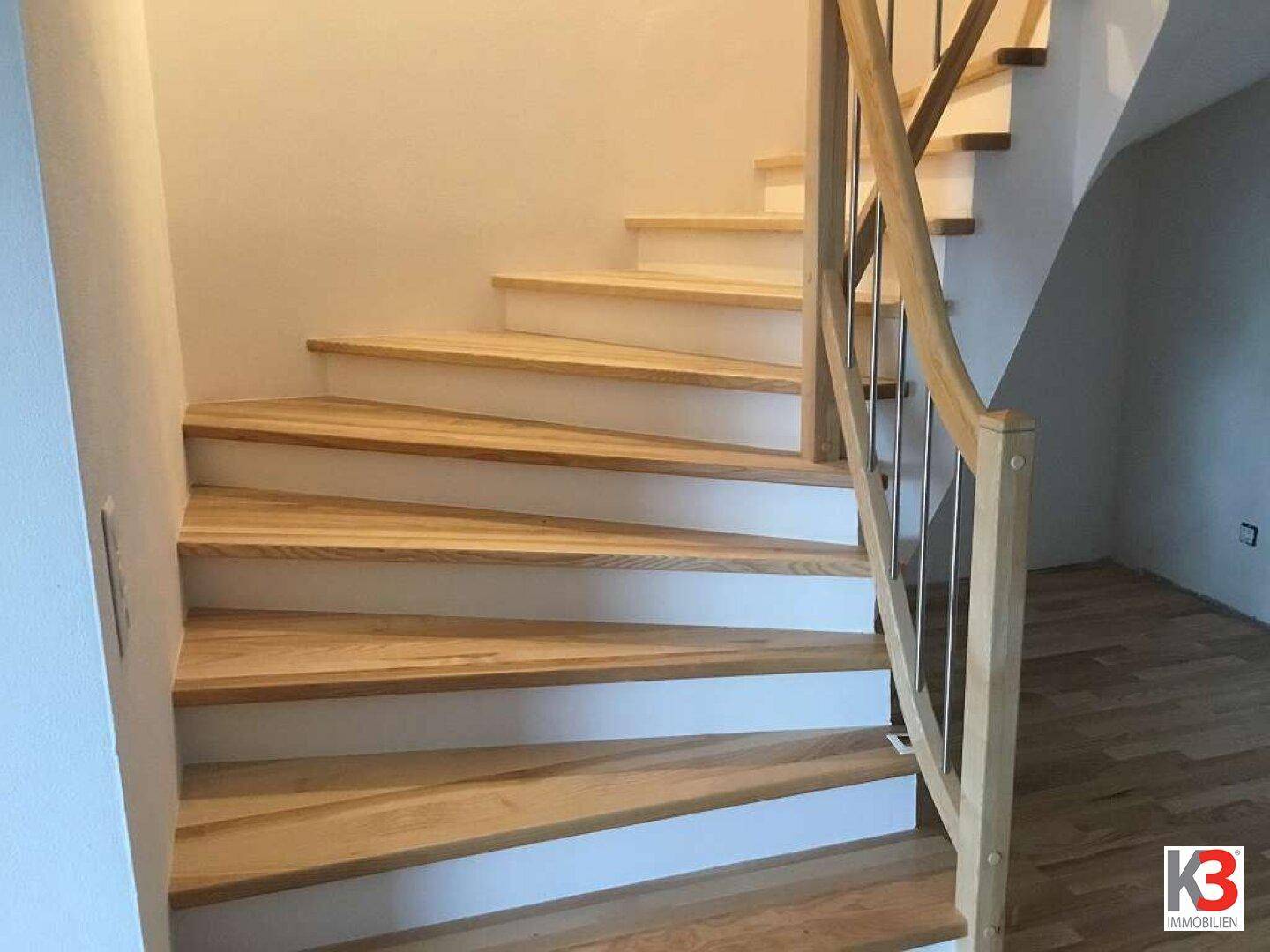 Moderne Holztreppe mit elegantem Geländer und hellen Wänden, die verschiedene Ebenen des Hauses verbindet.