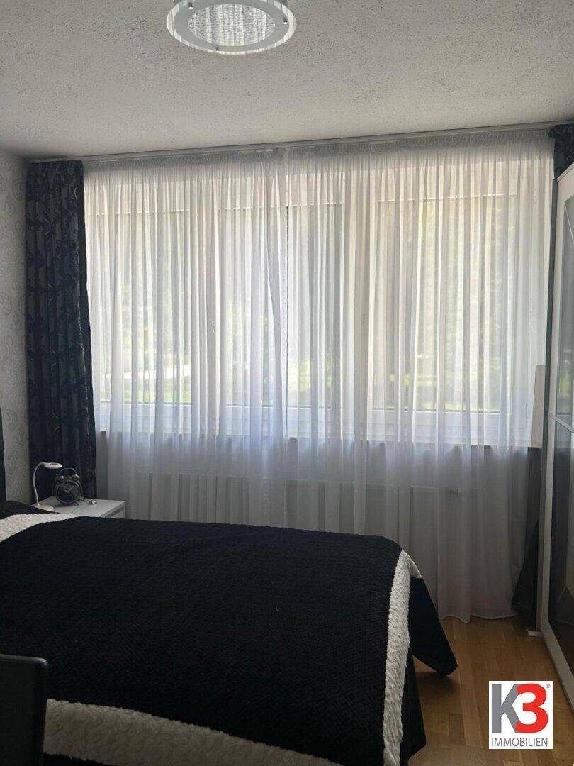 Schlafzimmer mit großem Fenster, das viel Tageslicht hereinlässt und einen Grünblick bietet.