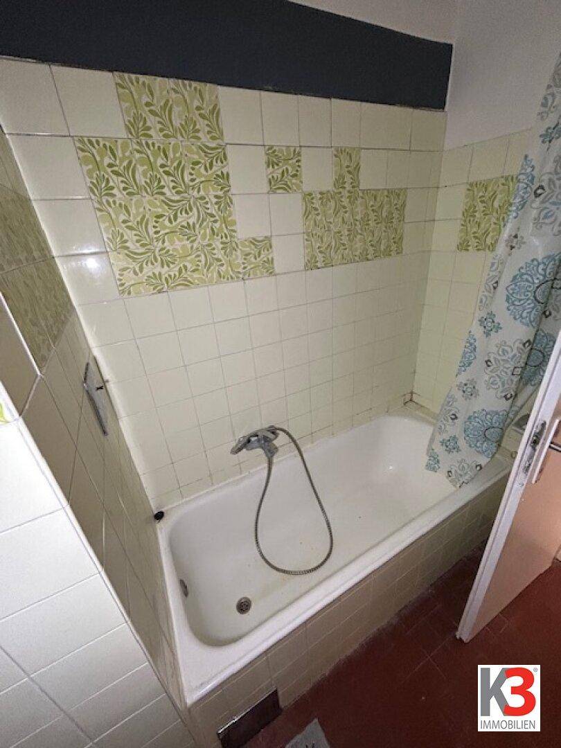 Badezimmer mit Badewanne und Wandfliesen im Stil der 80er Jahre mit grünen Mustern.