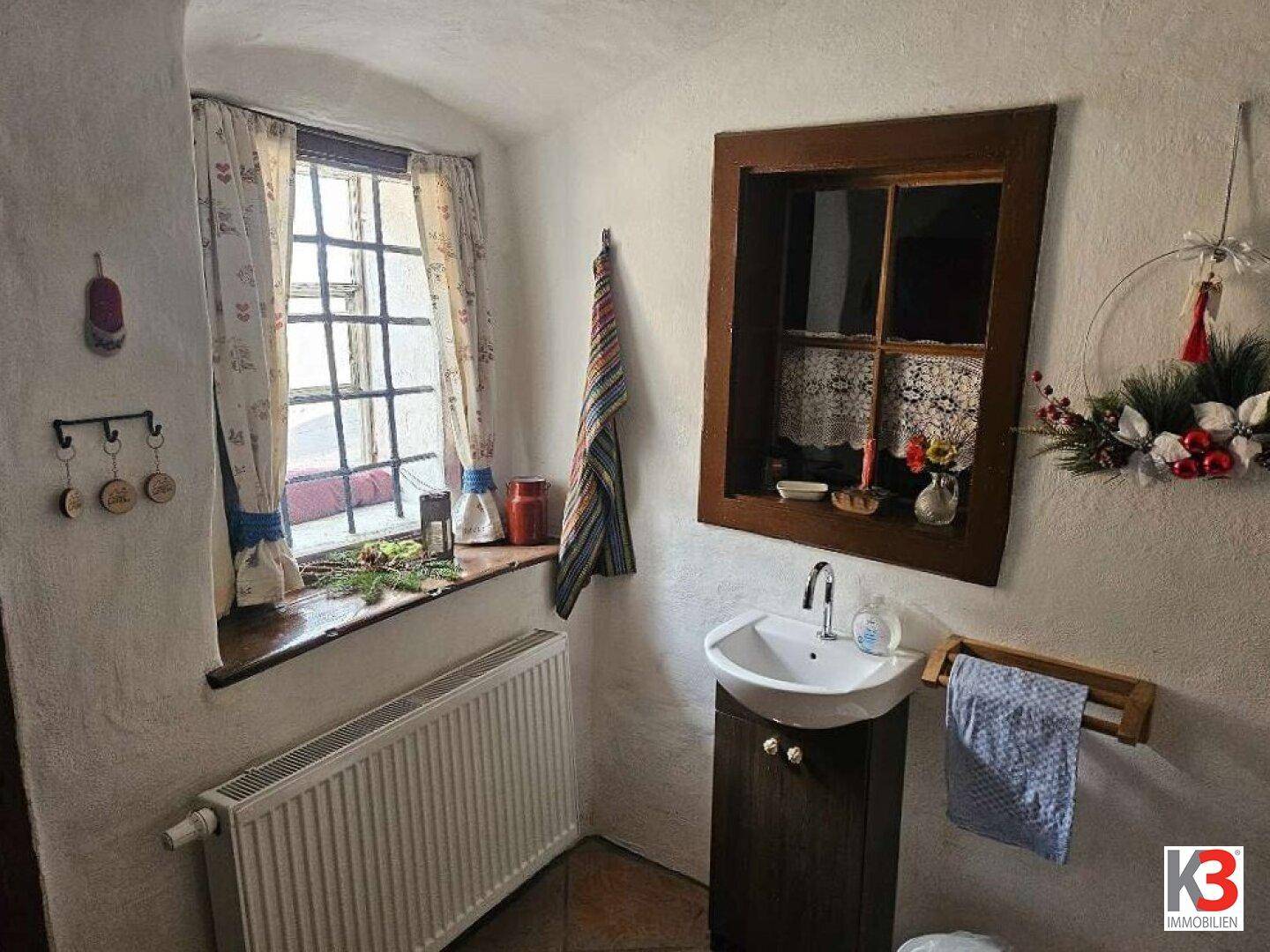 Kleines WC mit Fenster, Waschbecken und rustikalen Holzakzenten.