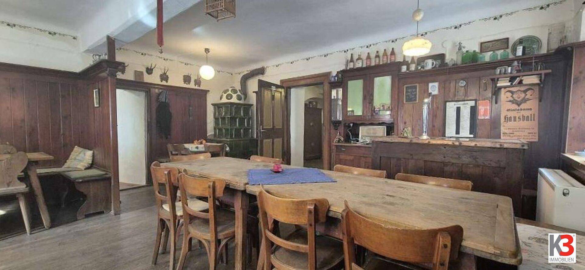 Traditioneller Essbereich mit Holztäfelung, großem Holztisch und einem Kachelofen.