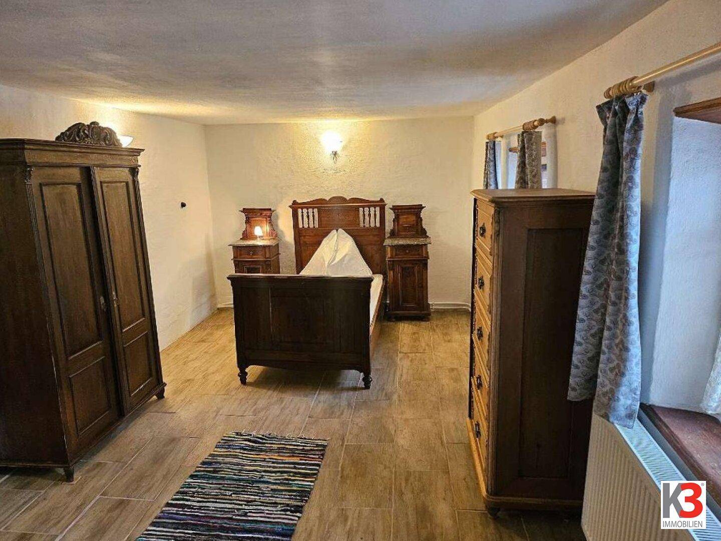 Rustikales Schlafzimmer mit dunklen Holzmöbeln, Fliesenboden und einem kleinen Teppich.