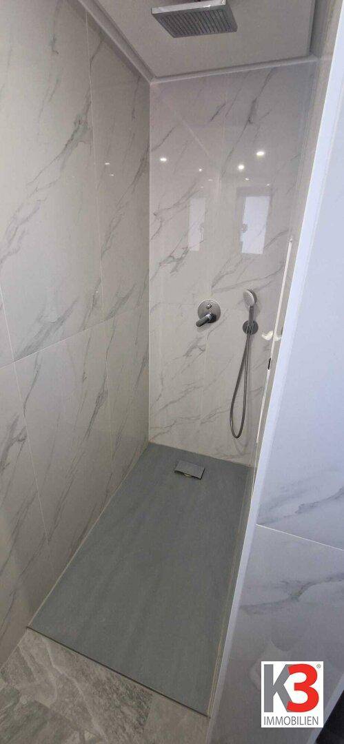 Moderne Duschkabine mit großformatigen Fliesen und Regendusche in hellem Badezimmer.