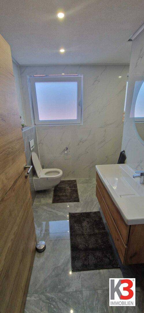 Badezimmer mit WC, Waschtisch und Fenster, ausgestattet mit modernen Fliesen.