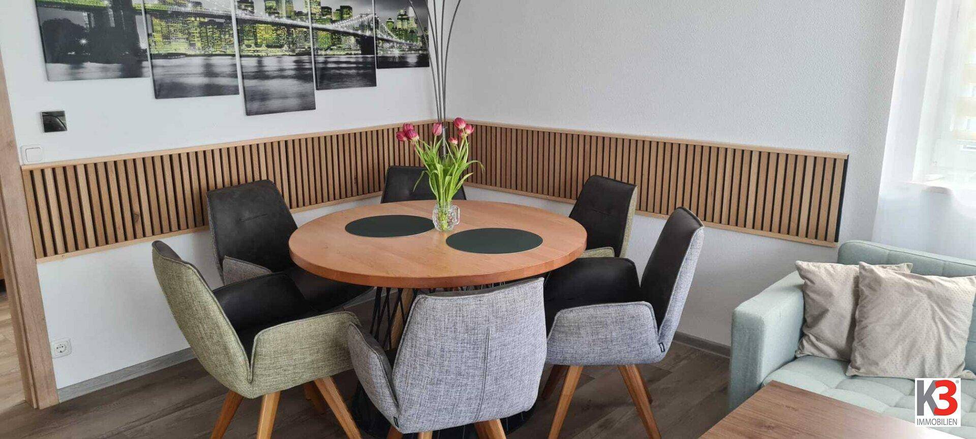 Gemütlicher Essbereich mit rundem Holztisch, modernen Stühlen und Wandverkleidung.