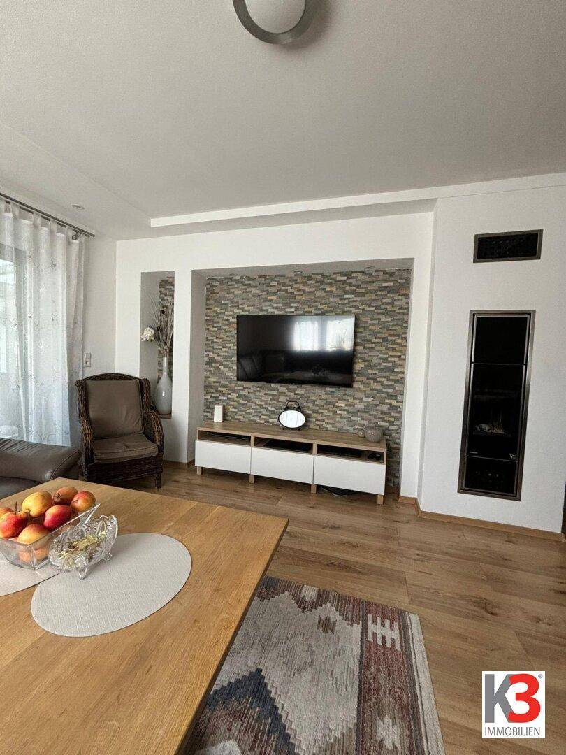 Wohnzimmer mit Fernseher an einer Steinwand, modernem Kamin und Holzboden.