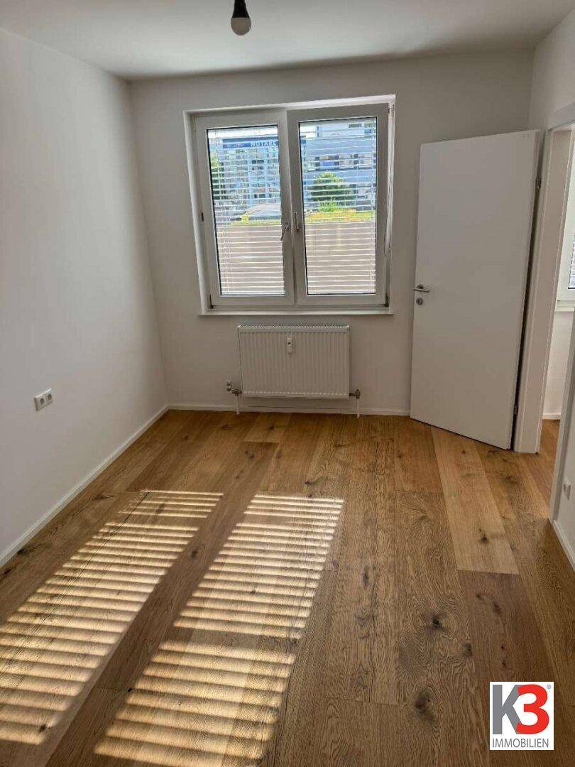 Helles Schlafzimmer mit Holzboden und großem Fenster, das viel natürliches Licht bietet.