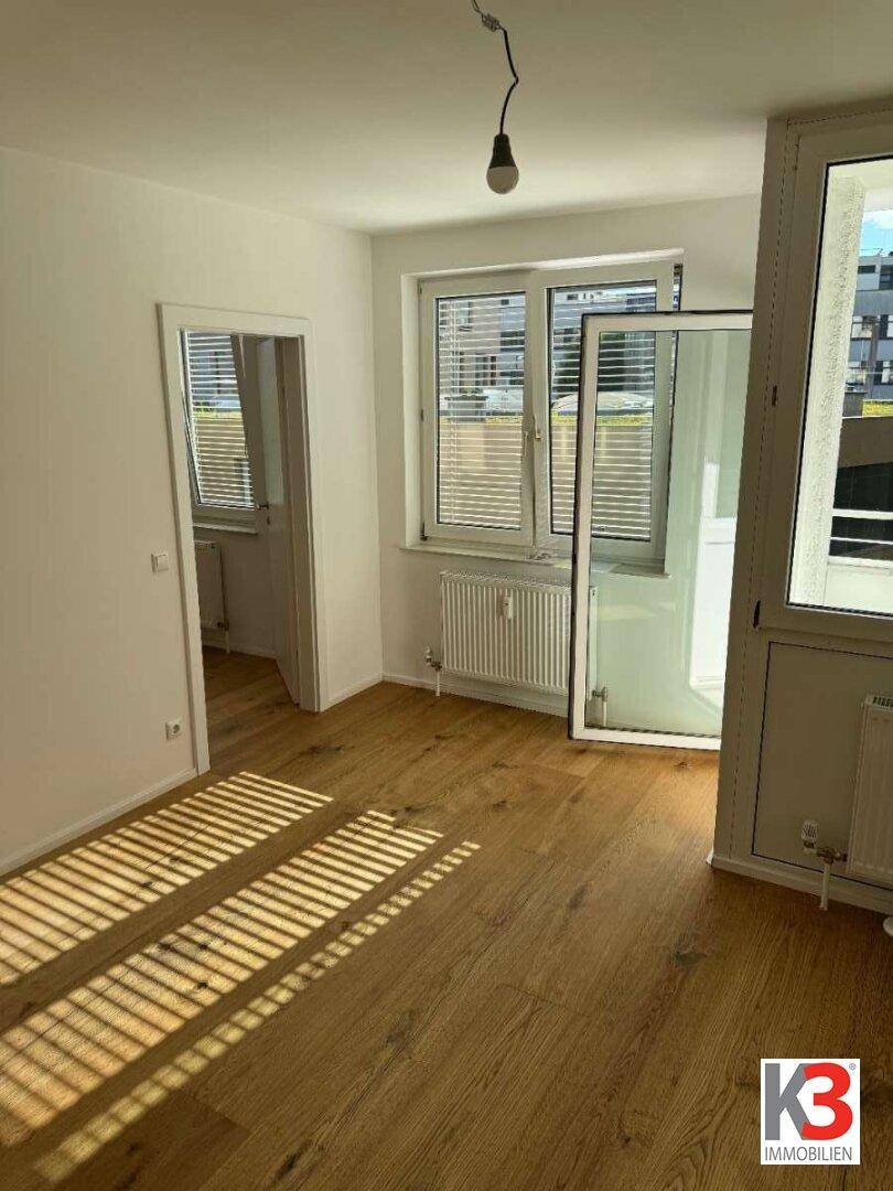 Lichtdurchfluteter Raum mit Holzboden und großen Fenstern, die viel Tageslicht hereinlassen.