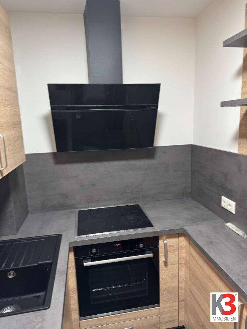 Moderne Küche mit dunkler Arbeitsplatte, Induktionskochfeld und integriertem Backofen.