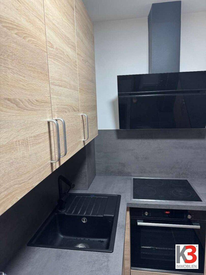 Detailansicht der modernen Küche mit Holzschränken, dunkler Spüle und integrierten Geräten.