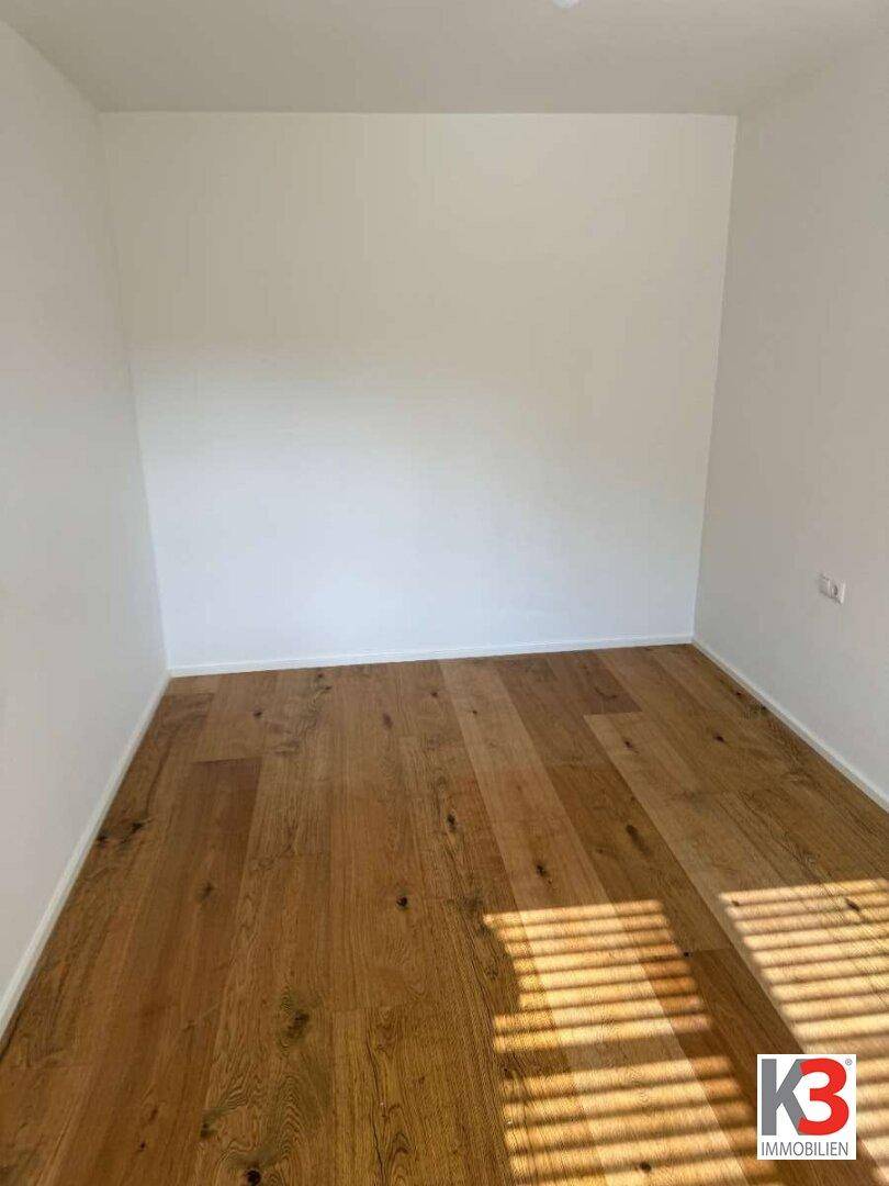 Leerer Raum mit Holzboden und weißen Wänden, bereit für individuelle Gestaltung.