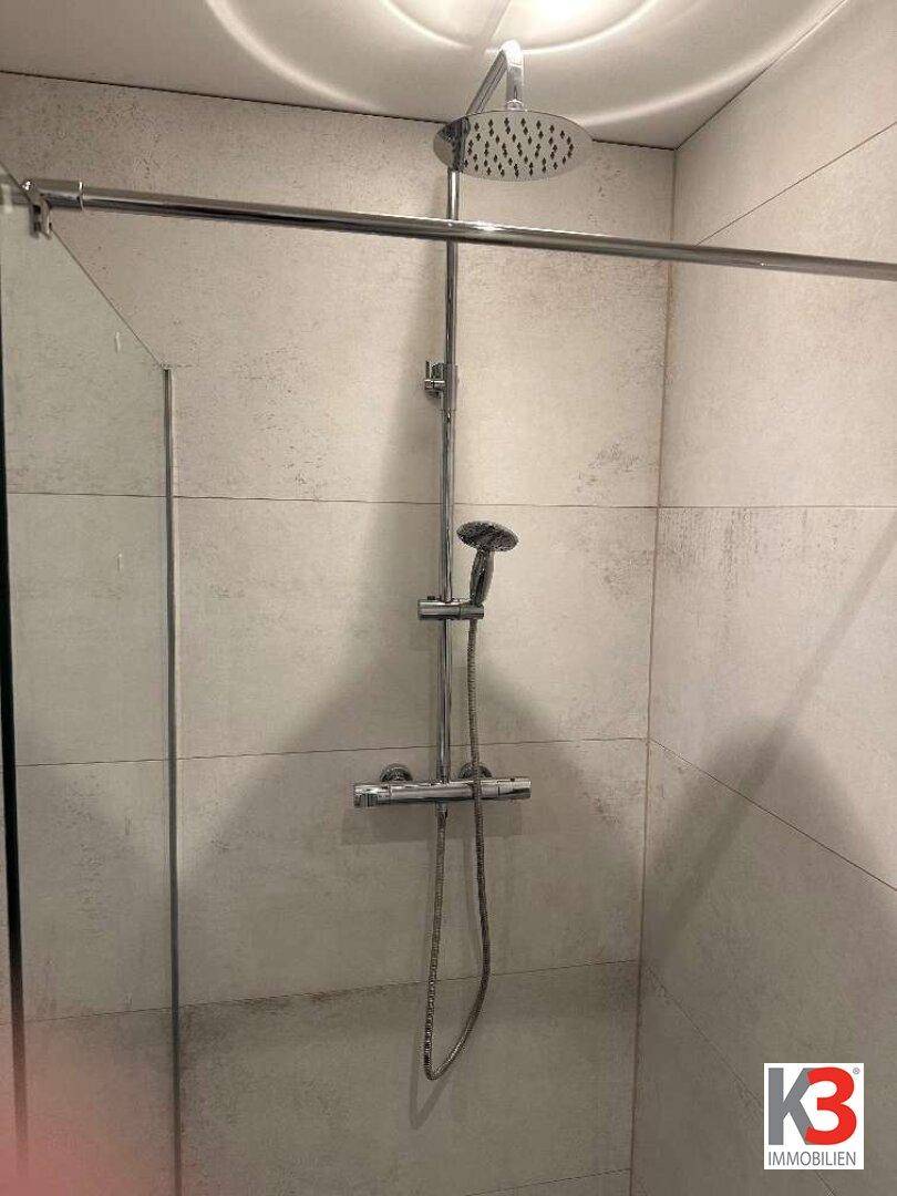 Duschbereich mit Regendusche und Handbrause, umgeben von modernen Fliesen.