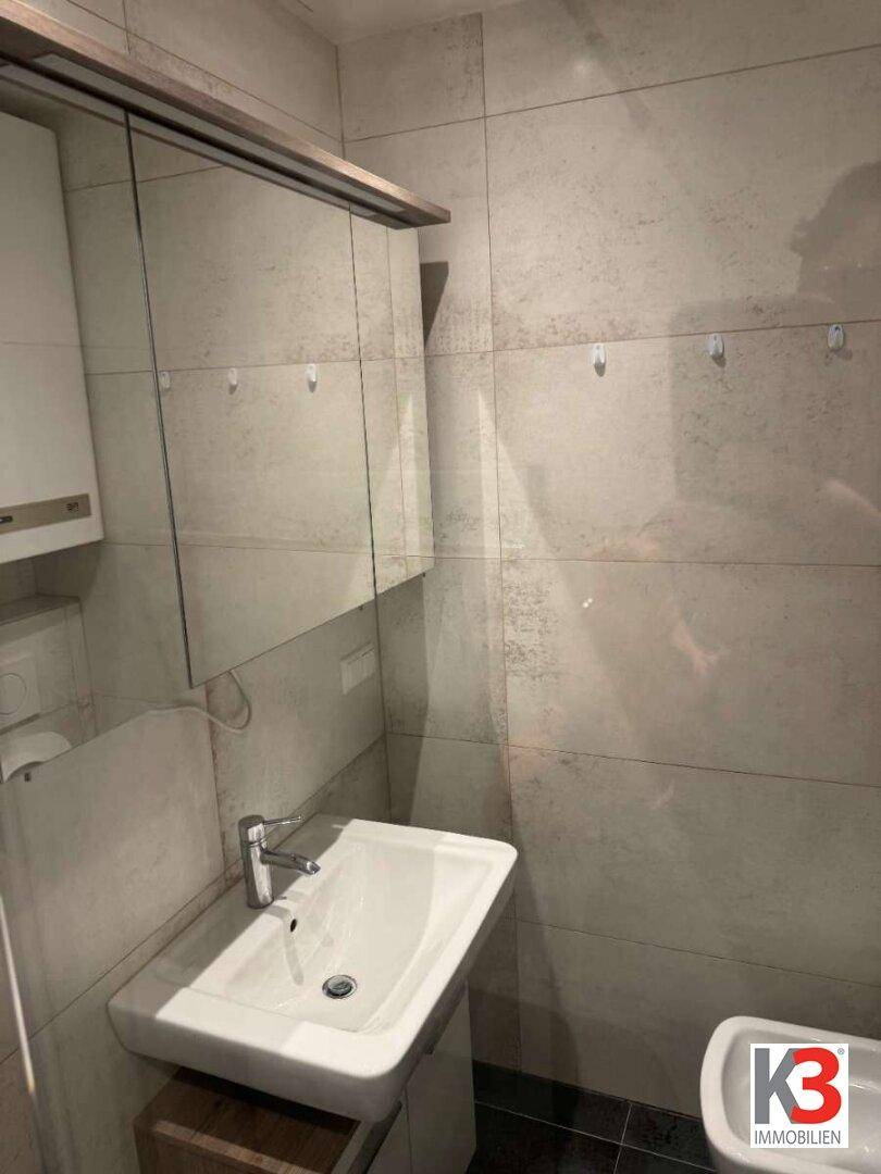 Modernes Badezimmer mit hellen Fliesen, Einzelwaschbecken und Spiegelschrank.