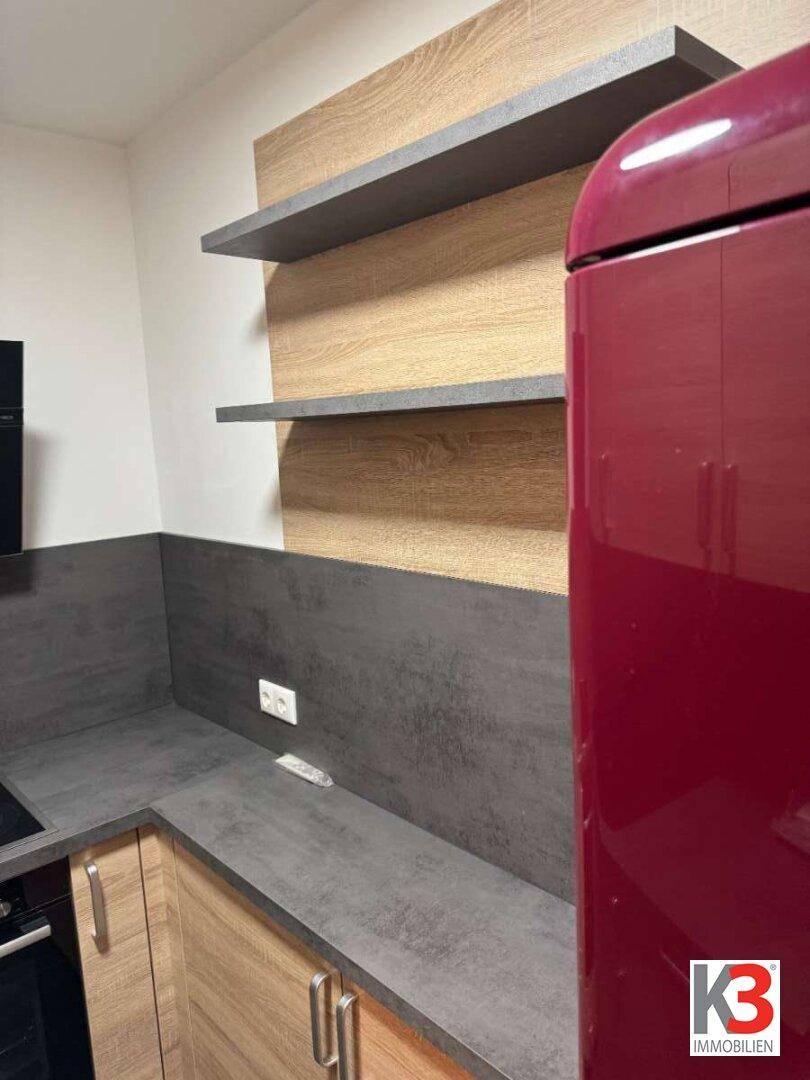 Küchenbereich mit offenen Regalen, dunkler Arbeitsplatte und einem auffälligen roten Kühlschrank.