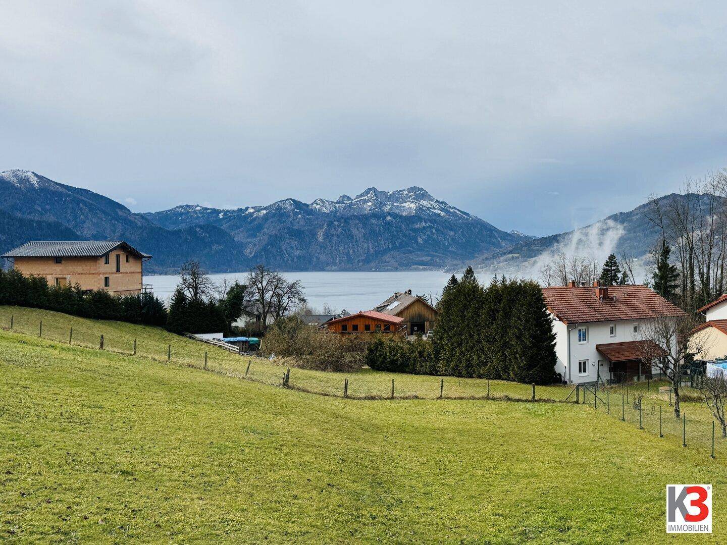 Panoramablick auf den See und die umliegenden Berge mit ländlicher Bebauung.