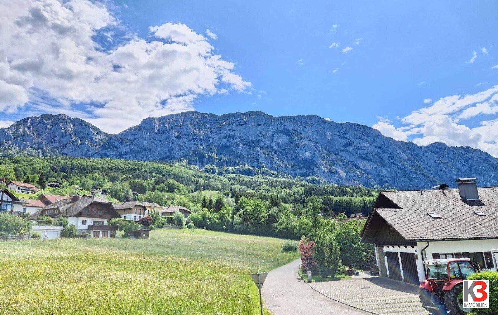 Weitläufiger Blick auf die majestätischen Berge und die grüne Landschaft mit vereinzelten Häusern.