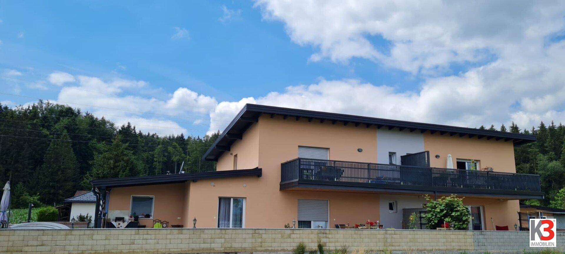 Rückansicht des Hauses mit großem Balkon und Blick auf bewaldete Hügel.