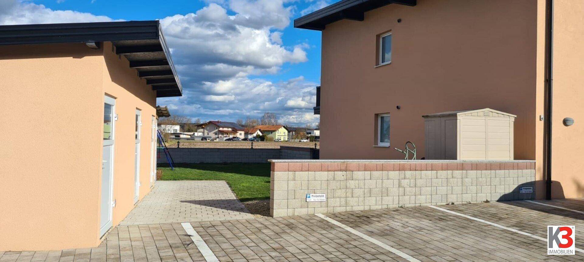Seitenansicht des Hauses mit gepflastertem Bereich und niedriger Steinmauer im Außenbereich.