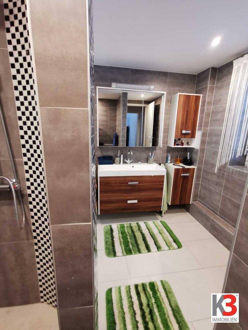 Das moderne Badezimmer mit Waschtisch, Spiegel, Holzmöbeln und Duschbereich.