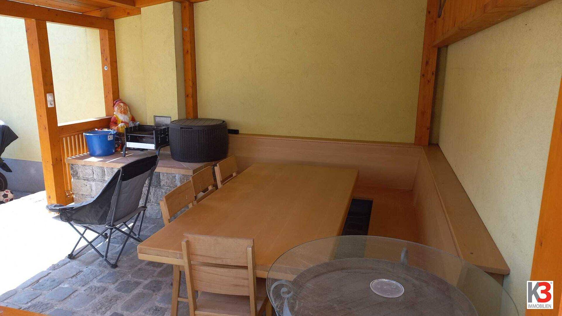 Die überdachte Terrasse mit Holztisch, Bänken, Pflasterboden und Gartenzwerg.