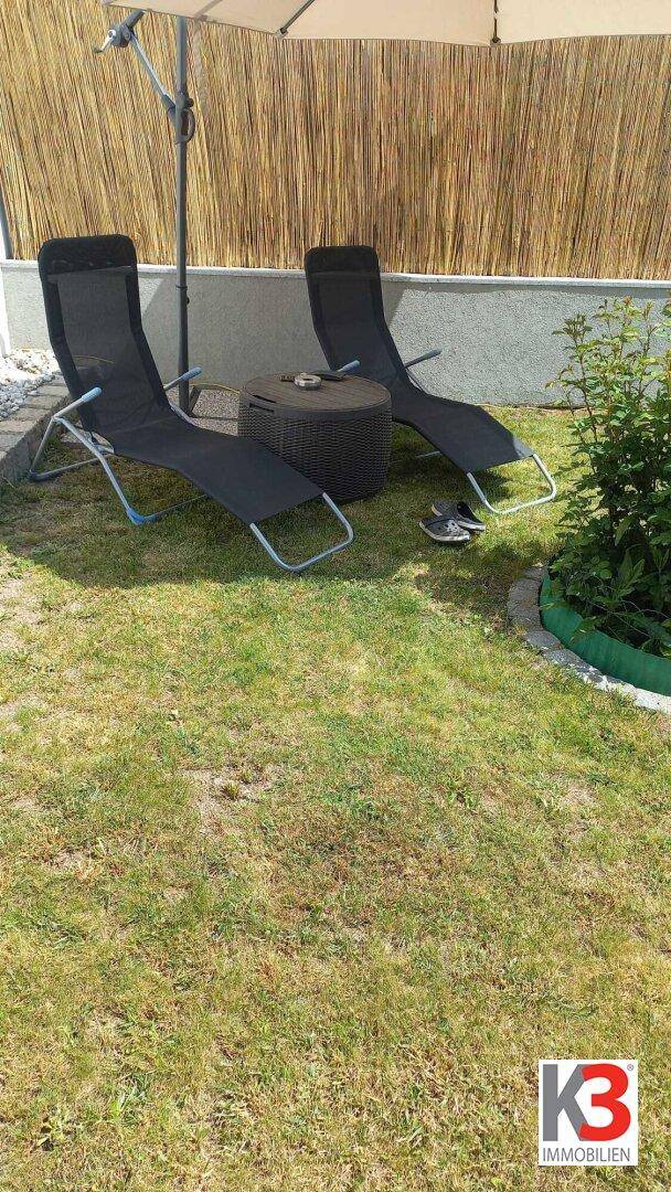 Ein sonniger Gartenbereich mit Liegestühlen, Sonnenschirm und einem natürlichen Bambuszaun.