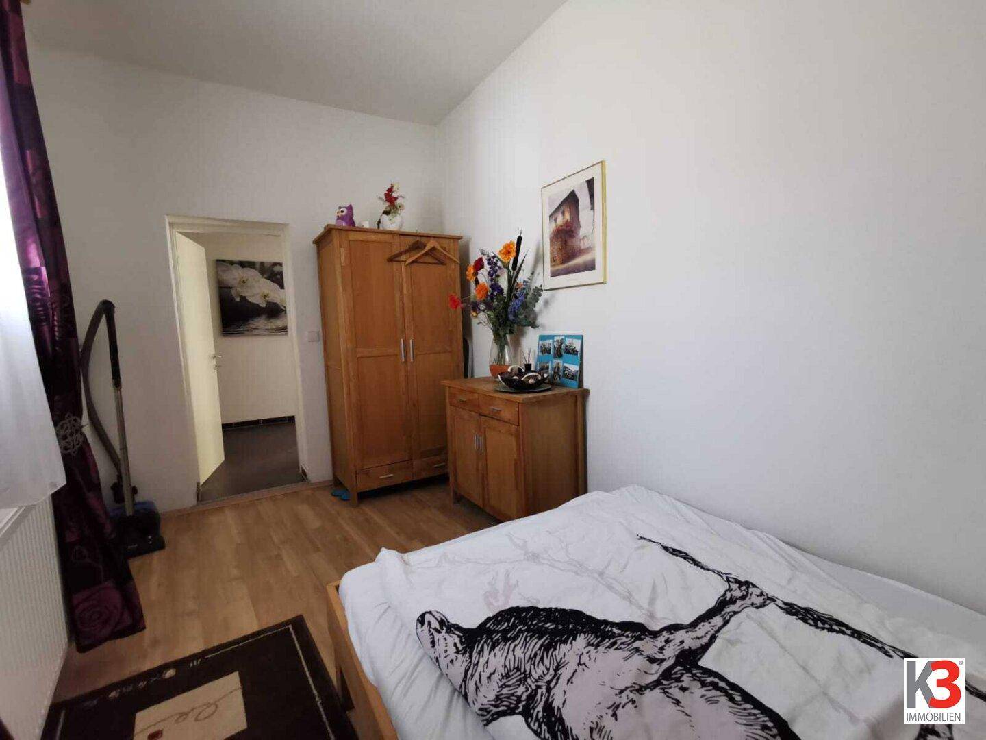 Das Schlafzimmer mit Einzelbett, Holzschrank und Blumenarrangement.