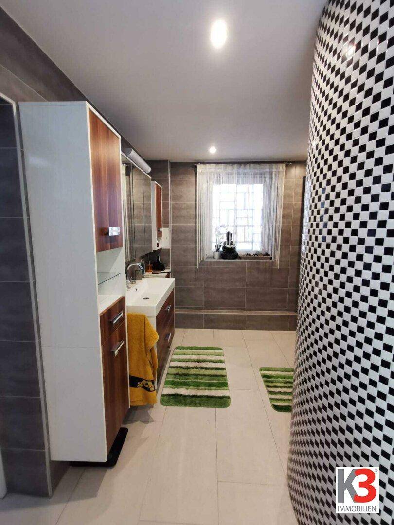Das moderne Badezimmer mit Waschtisch, Spiegel, Holzmöbeln, grauen Fliesen und Fenster.