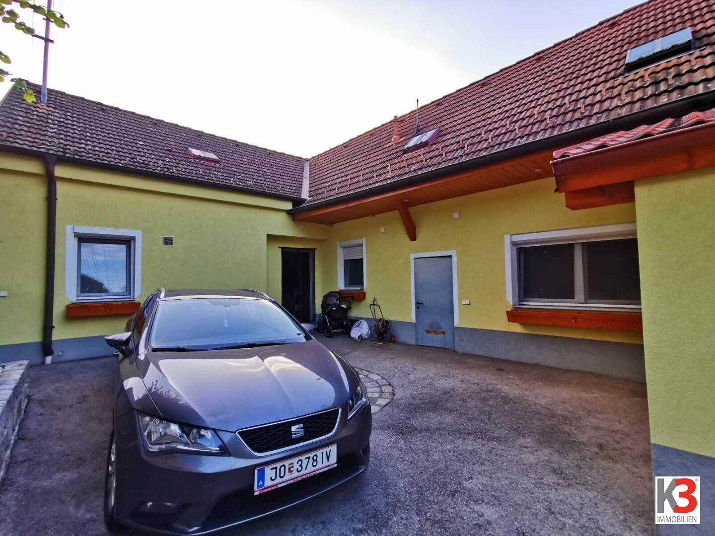 Der Hauseingangsbereich mit geparktem Auto und der gelben Fassade unter blauem Himmel.