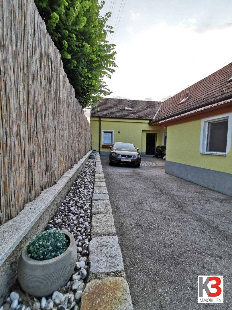 Die Einfahrt zum Haus mit einem dekorativen Kiesbeet und einem hohen Bambuszaun.